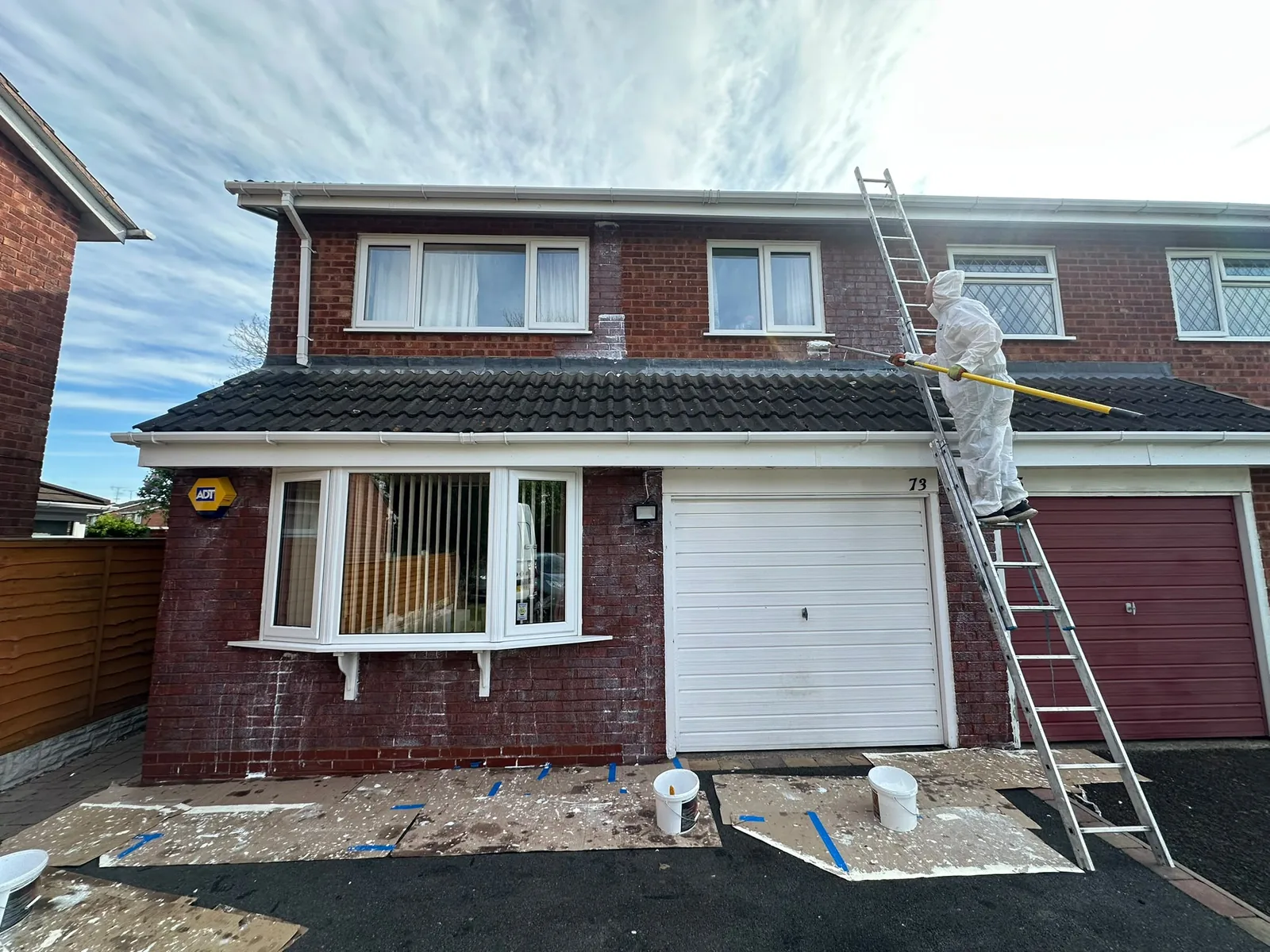 Apex worker on a ladder treating the rendered wall of a semi-detached house