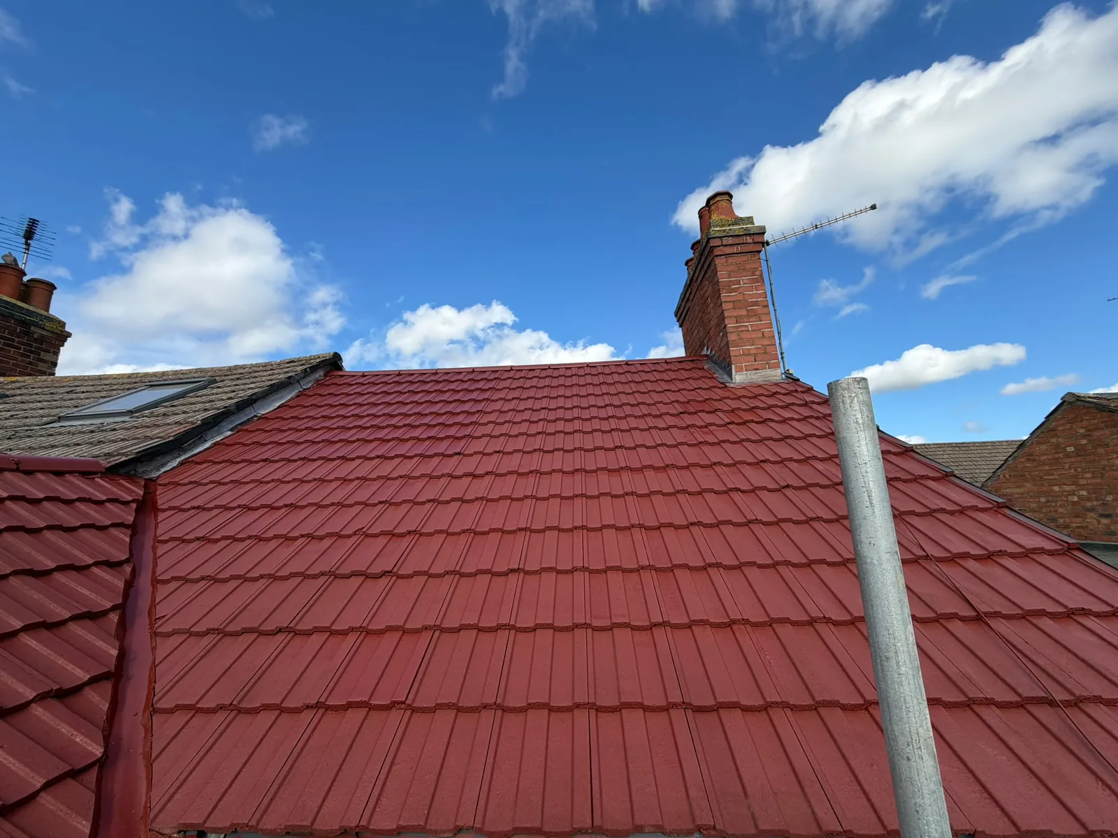 Newly tiled red roof with two brick chimneys under a blue sky