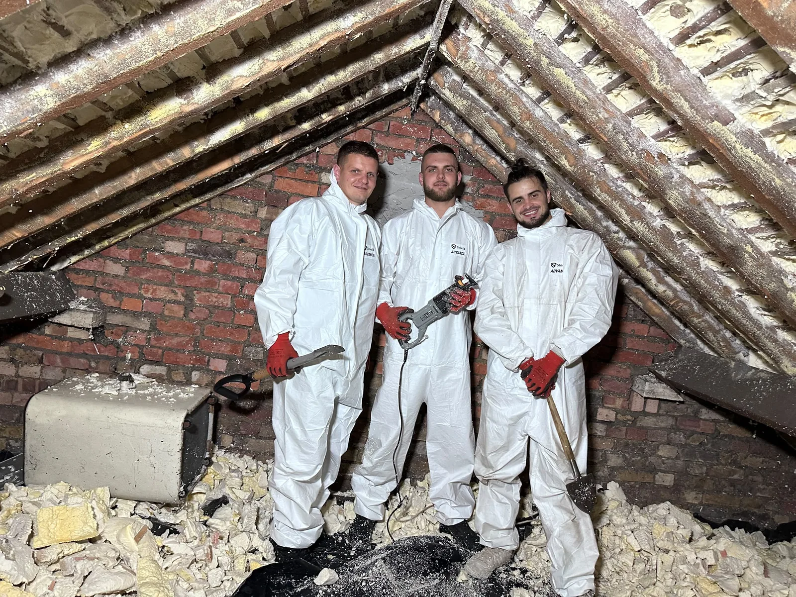 Three Apex technicians in protective suits, framed by the roof apex of a loft mid-removal
